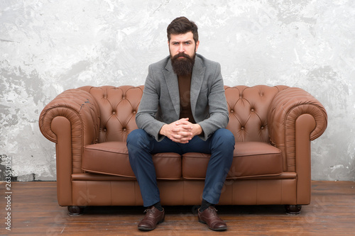 Classy but casual. Bearded man relaxing on sofa. Man or businessman wearing informal suit. Fashion man with long beard and trendy hairstyle. Brutal man following hipster lifestyle