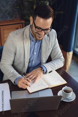 Above view of happy businessman writing down memos while working on a computer in the office