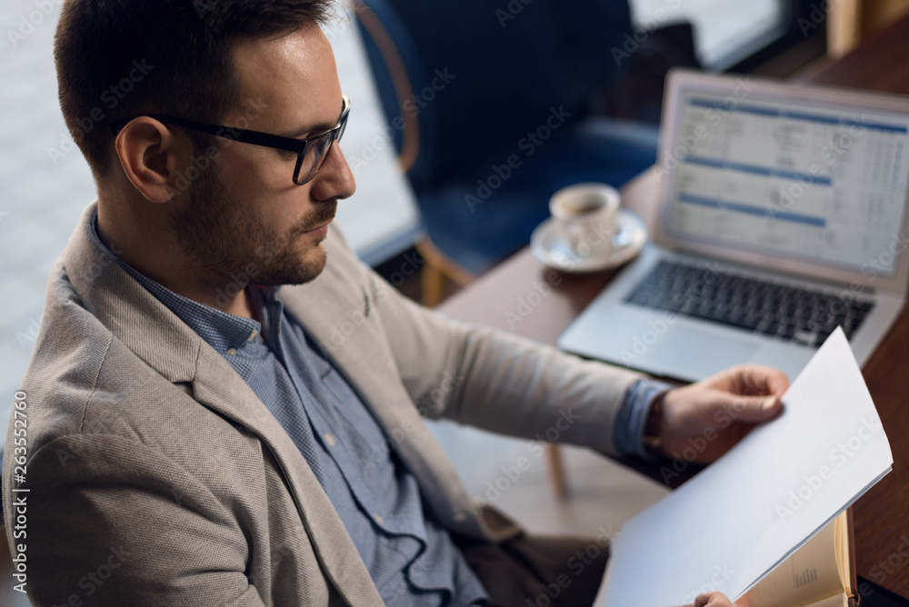 Profile view of serious businessman writing down memos while working computer in the office Profile view of serious businessman writing down memos while working computer in the office