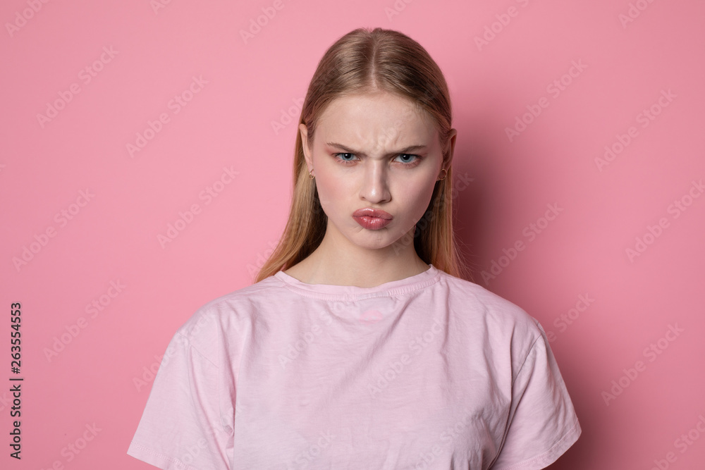 Fototapeta premium Portrait of cute young blonde girl looking angry at camera, having doubtful and indecisive face expression