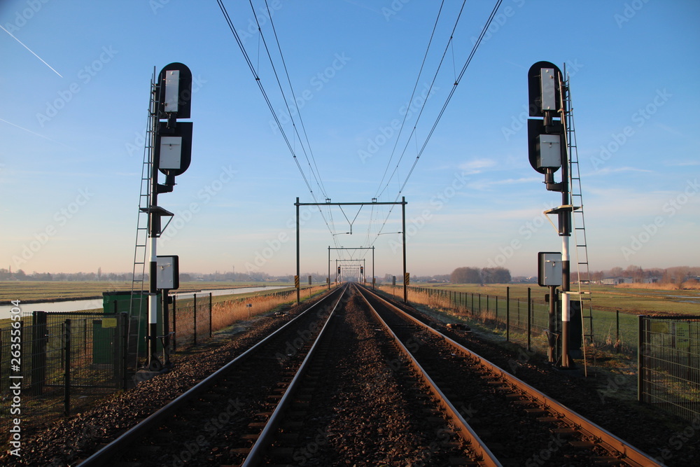 Railroad double track in Moordrecht during sunrise with signals in the low polder heading from Rotterdam to Gouda