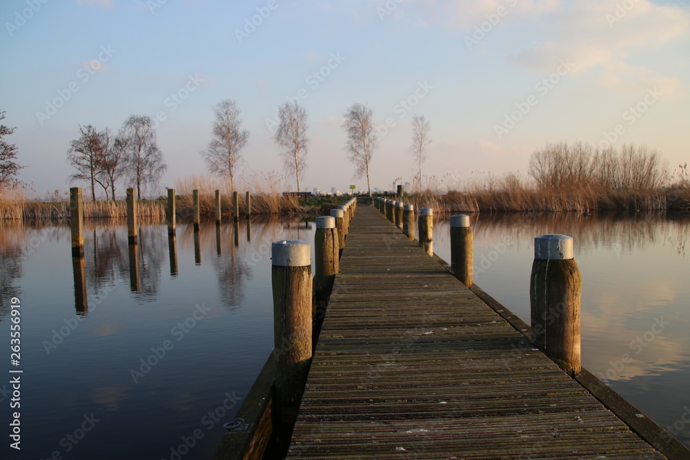 Naklejka premium Pier at the Rottemeren colored by the sunlight during sunset in Zevenhuizen
