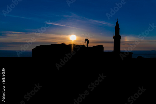 Silhouette of a photographer who shoots a sunset, on top of castle at sunset background.