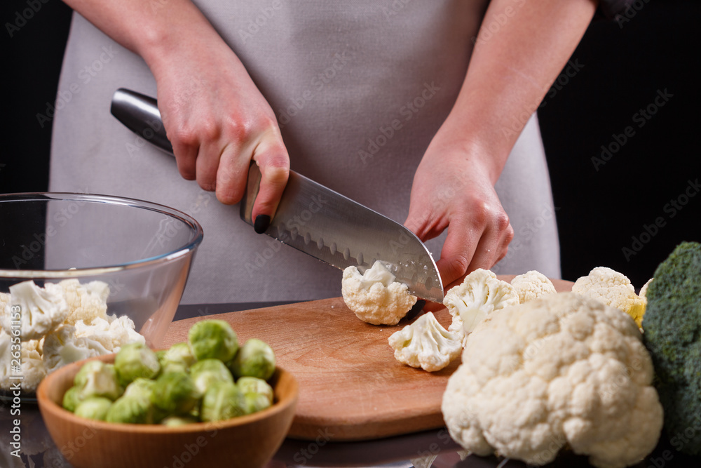 young woman in a gray aprons cuts cauliflower broccoli young woman in a gray aprons cuts cauliflower broccoli