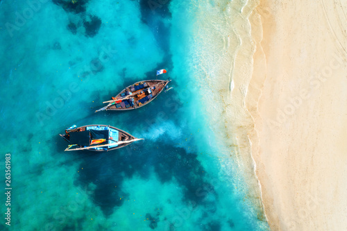 Aerial view of the fishing boats in clear blue water at sunset in summer. Top view from drone of boat, sandy beach. Indian ocean. Travel in Zanzibar, Africa. Tropical landscape with sailboats, sea © den-belitsky
