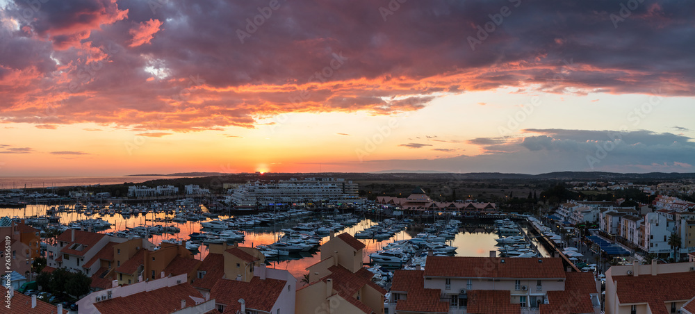 Aerial panoramic view of the Vilamoura marina in Portugal as the sunsets in the distance on a dramatic cloudy day.