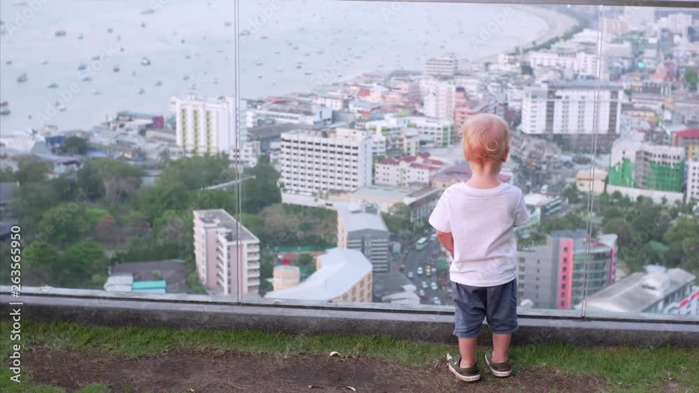 City view from a rooftop. Blond caucasian toddler is looking on a cityscape of Pattaya, Thailand. City view from a rooftop. Blond caucasian toddler is looking on a cityscape of Pattaya, Thailand.