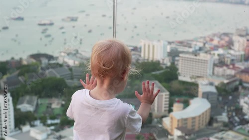 Two years old boy is looking on a cityscape of Pattaya, Thailand. Caucasianboy is enjoing the panorama view from the rooftop. photo