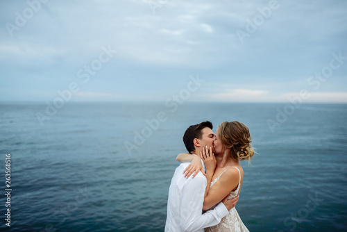 Happy bride and groom passionately kiss each other near the sea at sunset