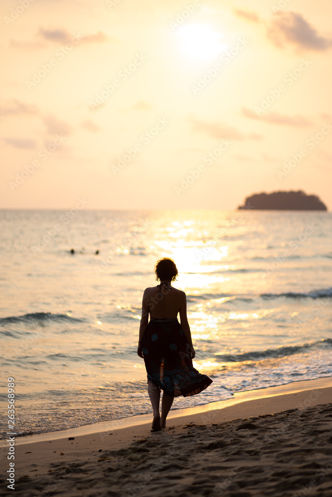 Beautiful woman in a colorful summer dress walking on the Thailand Ko Chang beach with beautiful white send during a sunset
