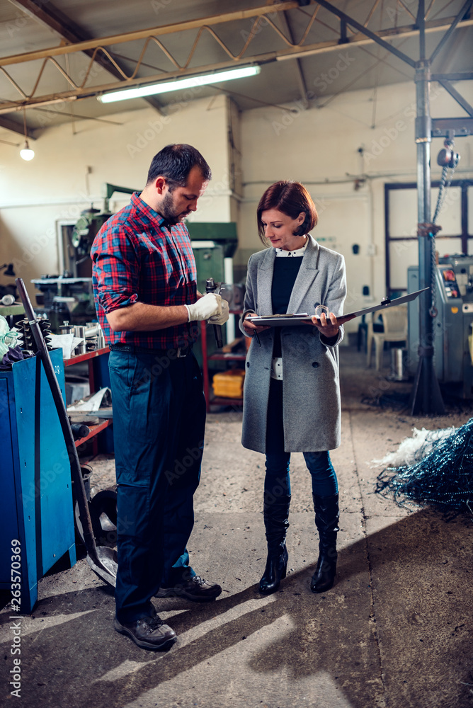 Female engineer consulting with machinist measuring gear shaft diameter