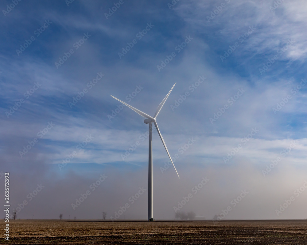 windmill rising above low hanging fog on a sunny morning in the countryside