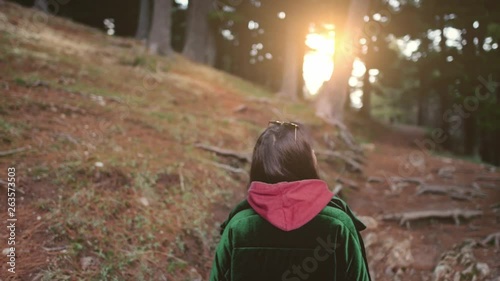 Teenage girl walking in the forest among pine trees at sunset