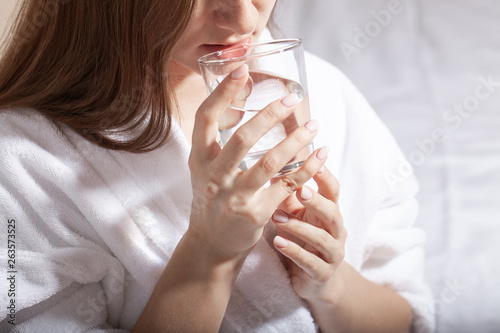 Young pretty european woman holding a glass and drink pure water sitting on the sofa. Cleansing the body of toxins. Healthy skin. Oily skin. Close up partrait of beautiful woman in bathrobe.