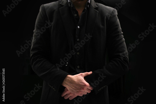 Portrait of a business man in a dark jacket and unbuttoned shirt who folded his arms on a black background. Male does not show face.