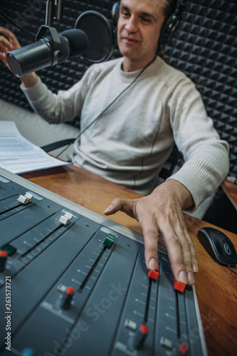 Happy smiling male radio presenter or host with headphones on head talking into microphone in radio station, portrait at workplace