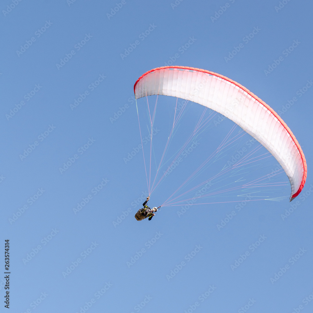 A man flies on a paraglider over green fields in the hot summer. Against the background of blue sky and rare clouds A man flies on a paraglider over green fields in the hot summer. Against the background of blue sky and rare clouds