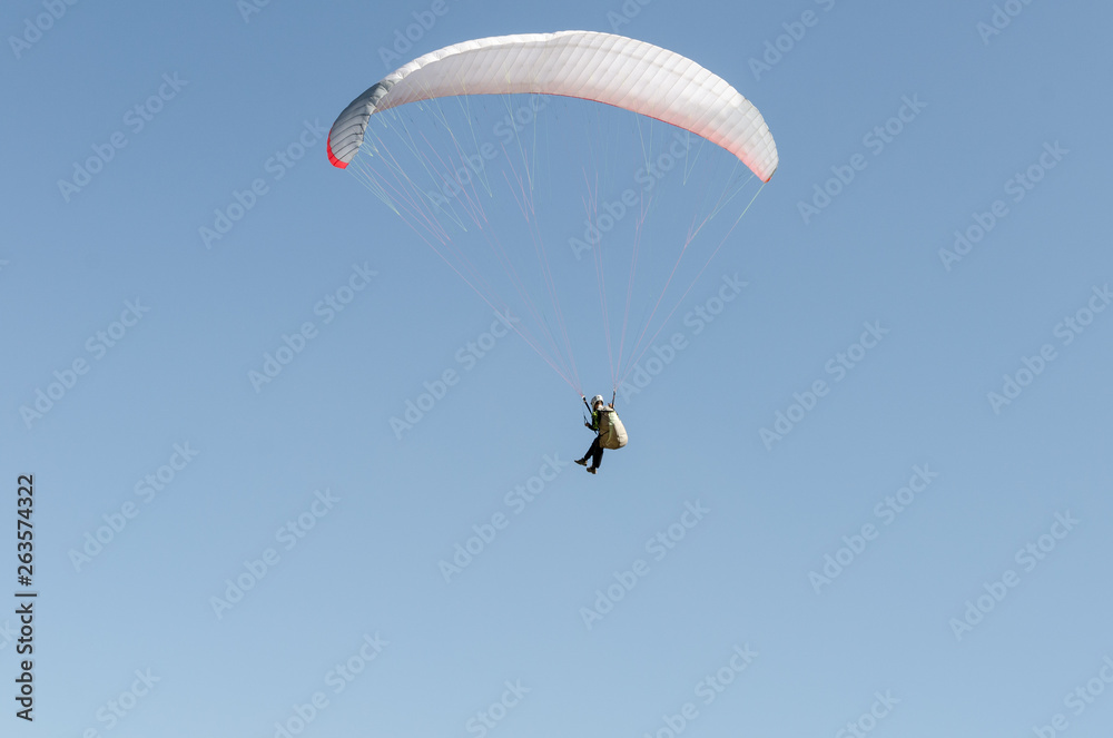 A man flies on a paraglider over green fields in the hot summer. Against the background of blue sky and rare clouds A man flies on a paraglider over green fields in the hot summer. Against the background of blue sky and rare clouds