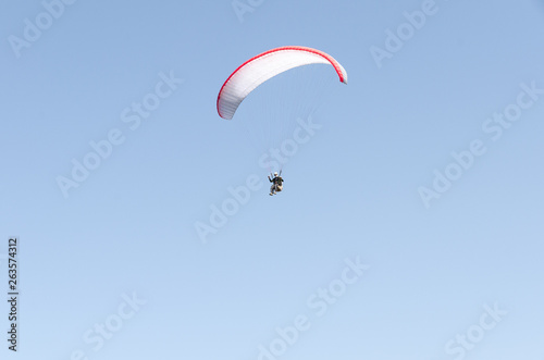 A man flies on a paraglider over green fields in the hot summer. Against the background of blue sky and rare clouds