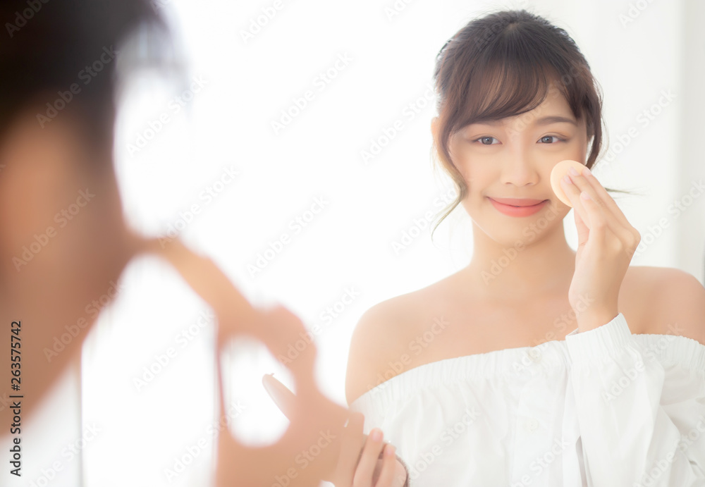 Portrait beautiful young asian woman applying powder puff at cheek makeup of cosmetic looking mirror, beauty of girl with skin face smile in the bedroom, health and wellness concept. Portrait beautiful young asian woman applying powder puff at cheek makeup of cosmetic looking mirror, beauty of girl with skin face smile in the bedroom, health and wellness concept.