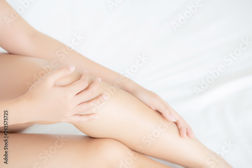 Closeup beautiful young asian woman sitting on a bed stroking legs with soft smooth skin in the bedroom  girl applying body cream and lotion with treatment care  healthy and wellness concept.