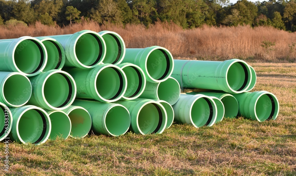 Large pile of empty water main pipes laying in a grassy background in the sunset. Large pile of empty water main pipes laying in a grassy background in the sunset.