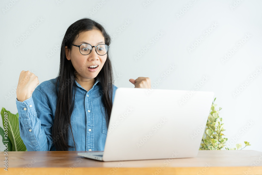 This asian woman is working on laptop in the office. On her face are expression surprise and happy to job success.