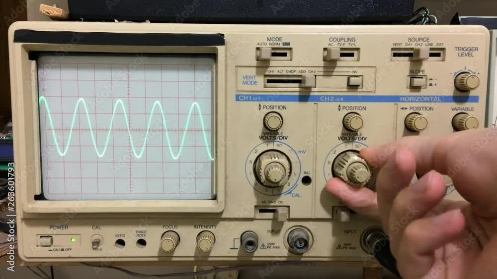Electronics working with oscilloscope and sine wave shown on oscilloscope