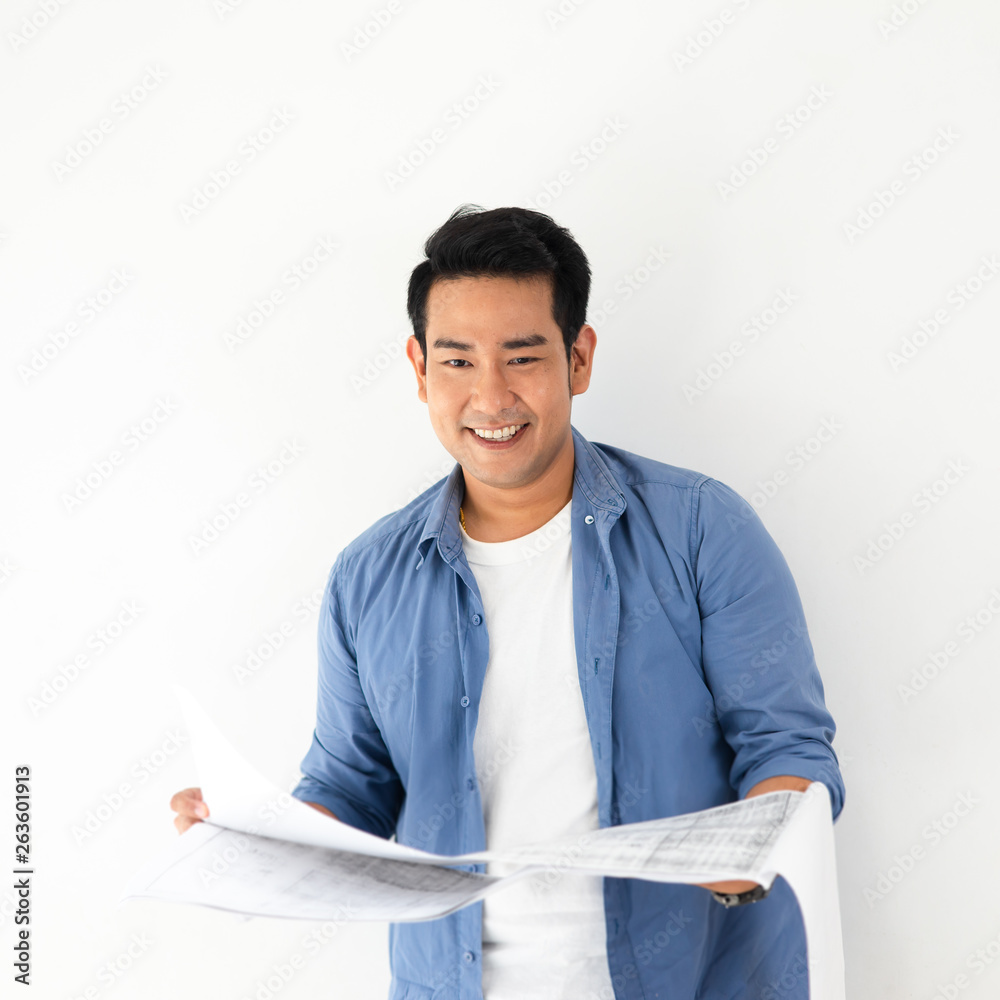 Happy ASian man looking at blueprint in his hands against white wall. Happy ASian man looking at blueprint in his hands against white wall.