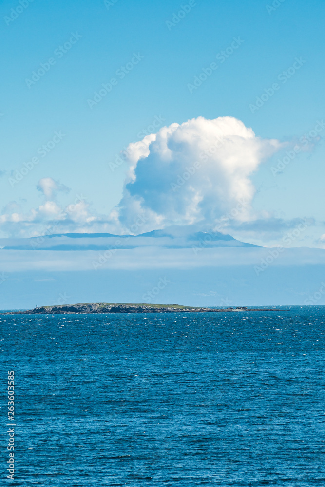 small island on the blue ocean with unique shaped cloud in the background under blue sky