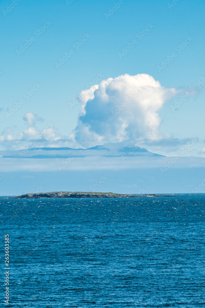 small island on the blue ocean with unique shaped cloud in the background under blue sky small island on the blue ocean with unique shaped cloud in the background under blue sky