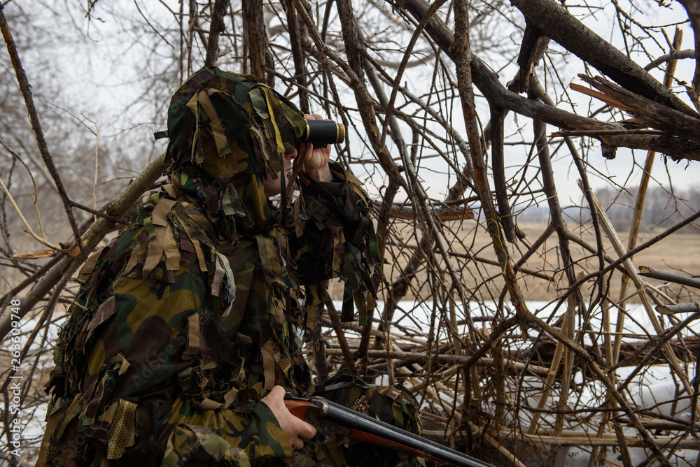 A hunter in a hut from the branches looks out for prey with binoculars. A hunter in a hut from the branches looks out for prey with binoculars.