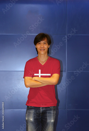 Man wearing Denmark flag pattern shirt and cross one's arm on the blue wall background, photo
