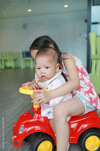 Asian Sister and little baby boy enjoying riding on a small toy car at playroom.