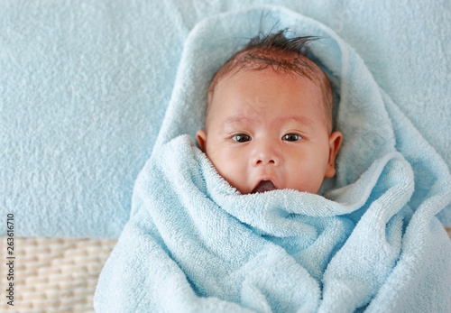 Portrait of Infant baby boy in towel roll looking at camera lying on bed after bath. Above view.