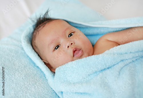Portrait of cute infant baby boy in towel lying on bed after bath.