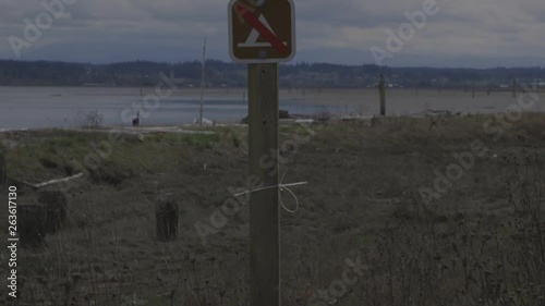 English Boom Preserve. Camano Island, WA. Official Park sign. No Camping. No Fires. No Vehicles. Panning shot from lower part of wooden signpole to brown, metal signs. photo