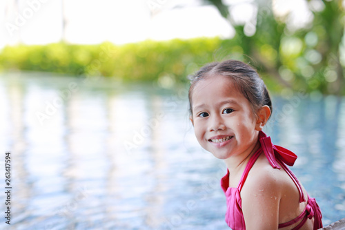 Cute little Asian child girl in a mermaid suit has fun sitting poolside.