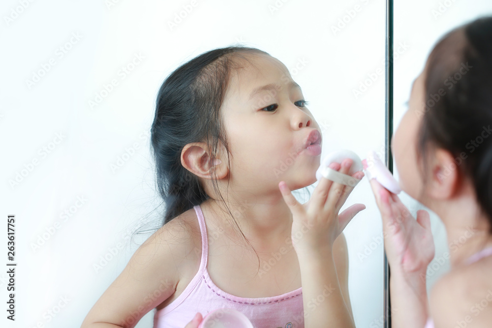 Cute little child girl applying makeup on face with Sponge Powder Puff near a mirror. Kid make up herself. Cute little child girl applying makeup on face with Sponge Powder Puff near a mirror. Kid make up herself.