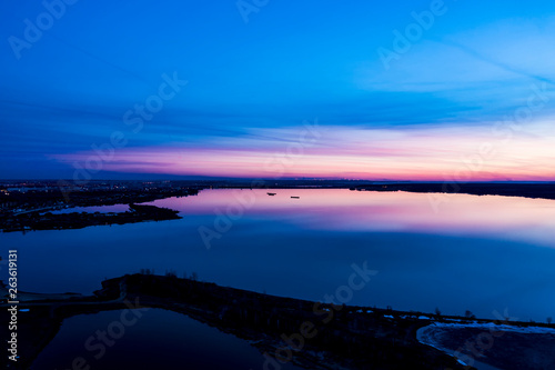 A quiet spring evening. Sunset over the river. It shows a purple sky, a purple reflection on the water, in the distance you can see the lights of the city. The view from the top. Copy space.