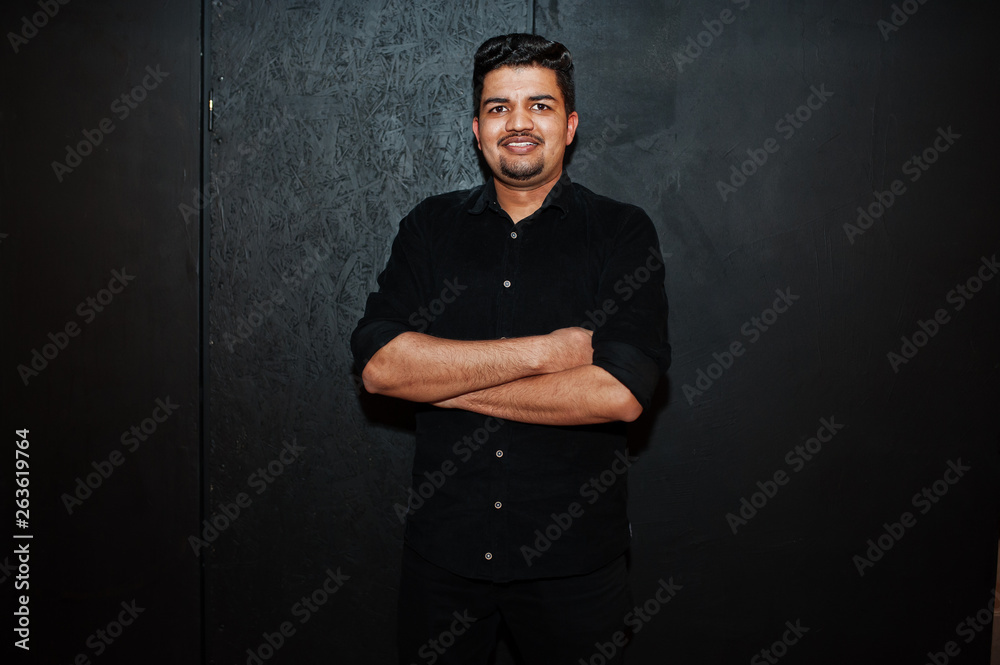 Asian man in black shirt on dark background posed with crossed arms.
