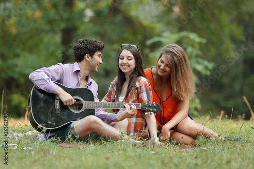 group of students with a guitar relax sitting on the grass in the city Park © yurolaitsalbert