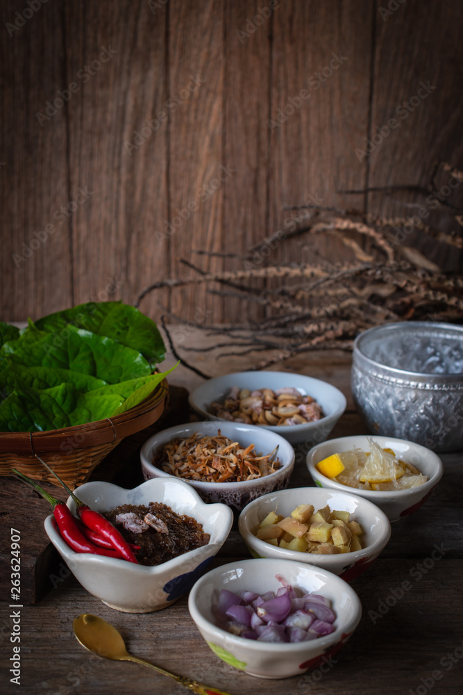 Miang kham,A royal leaf wrap appetizer Consist of Shallot, Ginger, Fried beans, Slice of lemon, Betel leaf, Chilli, Fried coconut and chili sauce, whole placed on the wood table. Miang kham,A royal leaf wrap appetizer Consist of Shallot, Ginger, Fried beans, Slice of lemon, Betel leaf, Chilli, Fried coconut and chili sauce, whole placed on the wood table.