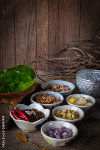 Miang kham,A royal leaf wrap appetizer Consist of Shallot, Ginger, Fried beans, Slice of lemon, Betel leaf, Chilli, Fried coconut and chili sauce, whole placed on the wood table.