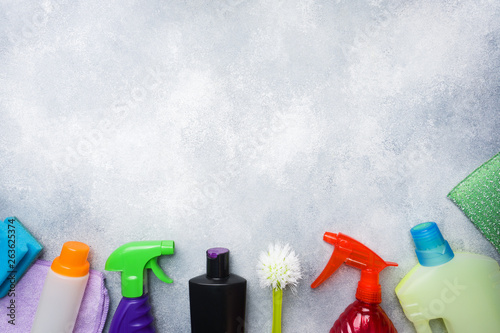 Bottles with detergents, brushes and sponges on concrete background. Colorful cleaning products. Home cleaning concept. Top view, copy space.