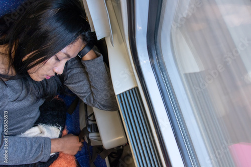 Young woman sleeping on a train by the window, look from above. A tired passenger relaxes in a driving train with a passing way behind the window. photo