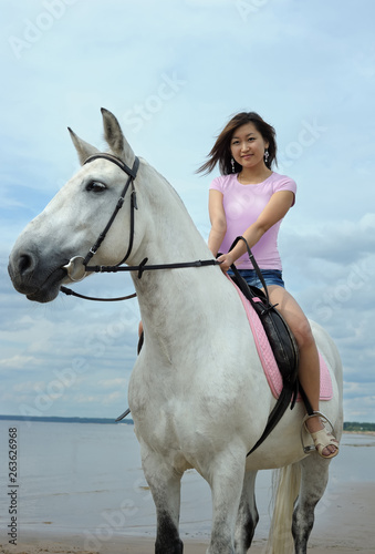 Young asian woman riding white horse on the beach
