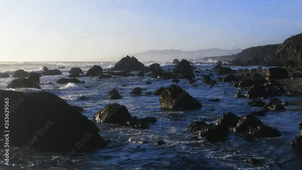 Drone captures a setting sun at golden hour over empty a rocky beach and surf break. Haze and setting sun create a dreamy and surreal vibe.