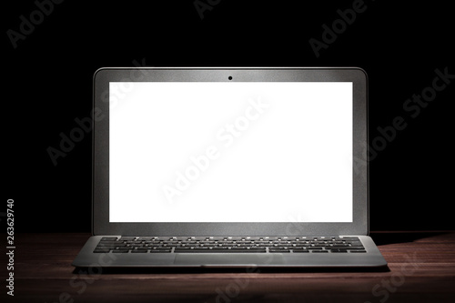 One silver modern laptop with empty white screen on wooden table in a dark room on black background. Nice mockup for your IT project. Dramatic light.