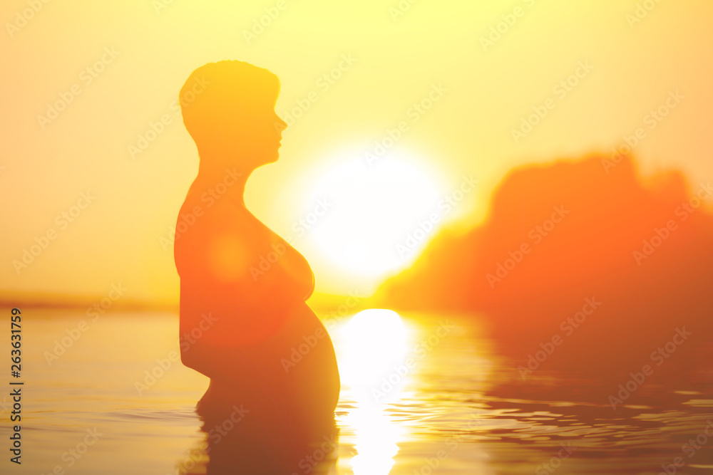 Silhouette of a pregnant woman in the water during sunset